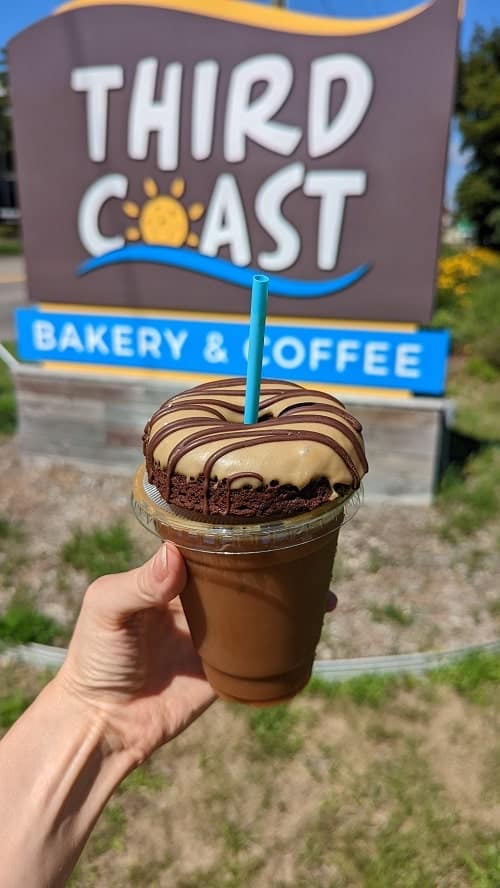 vegan mocha donut sittting on top of an iced coffee in front of the third coast sign in traverse city
