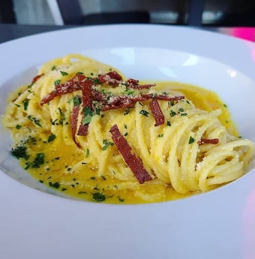 white bowl filled with creamy vegan carbonara and topped with tiny pieces of vegan bacon and herbs in philadelphia