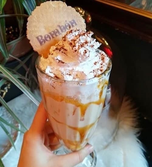a large sundae glass filled with vanilla vegan milkshake, a caramel swirl and topped with a bombon cookie  in madrid