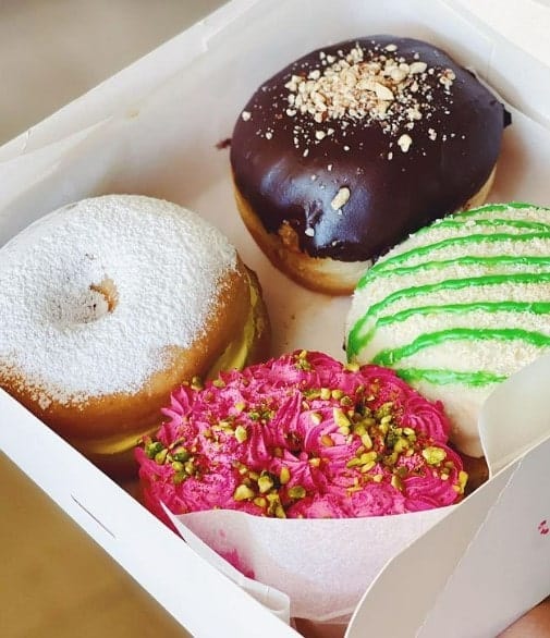 a box of four vegan donuts topped with dark chocolate, bright pink icing, white icing, and a lime green drizzle  in madrid