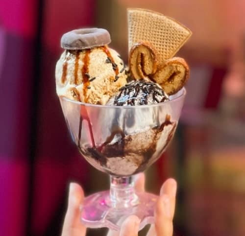 a vegan ice cream sundae in a glass cup with vanilla ice cream, chocolate sauce, and three kinds of cookies in madrid