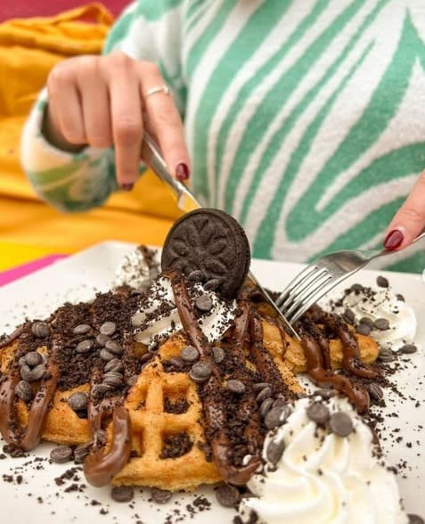 giant stack of golden vegan waffles covered in chocolate sauce and chocolate cookies with someone cutting into it  in madrid