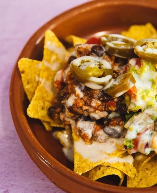 loaded vegan nachos covered in yellow queso in a red bowl in madrid