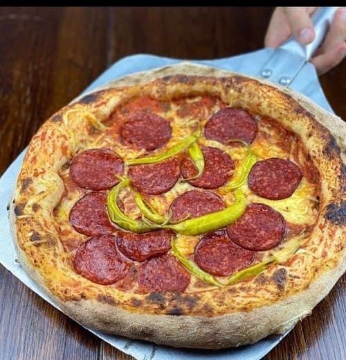 large vegan pizza with a golden crust covered in a ring of red pepperoni and a few green chilis in madrid