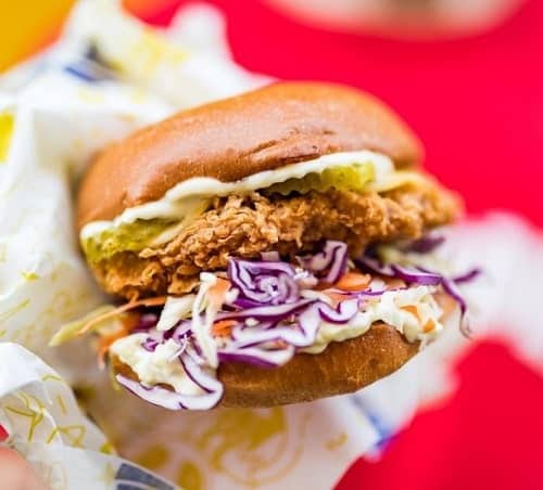 one hand holding a large vegan golden fried chicken sandwich topped with cabbage, pickles, and sauce in madrid