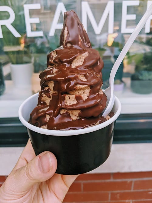 cup of chocolate vegan soft serve topped with a dark chocolate shell in front of the vaca's creamery sign in chicago
