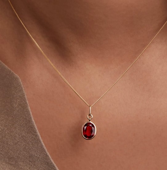 a gold chain necklace with a small ruby pendant from mejuri