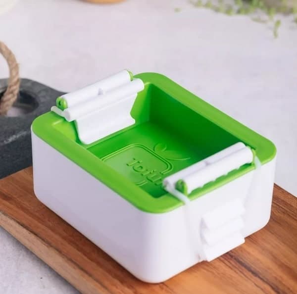 a green and white tofu press sitting on a wood cutting board