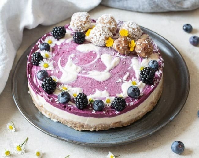 one large round vegan cheese cake topped with a light purple blueberry sauce, blueberries, black berries, and a white cream in vienna