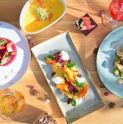 four different shaped dishes filled with bright veggies and fruit on a light wood table at yamm in vienna