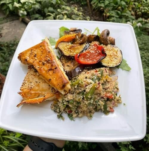 a white plate filled with two vegan tofu triangle steaks, quinoa salad, and roasted vegetables in krakow