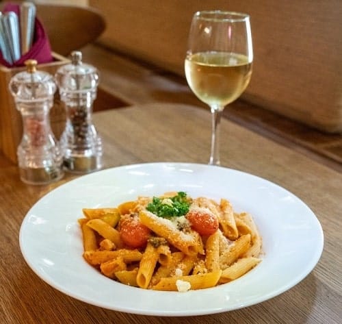 white bowl filled with vegan tomato pasta and topped with basil with a glass of white wine next to it in prague