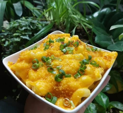 a small rectangle bowl filled with creamy vegan mac and cheese and topped with green onions in front of greenery in prague