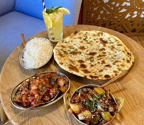 two small silver dishes filled with vegan indian food and one large vegan naan bread on a light wood table in krakow