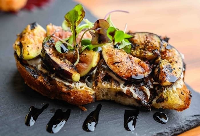 two vegan fig and balsamic toasts on a black slate plate at blossoms in nyc