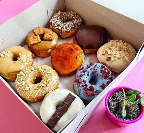 a boxof 12 colorful vegan donuts sitting on a hot pink table in prague