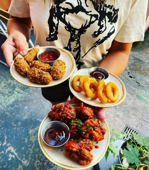 one person holding three plates with vegan onion rings, cauliflower wings, and fried cheese in munich
