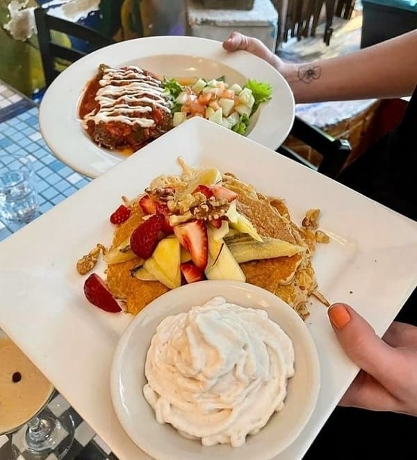 a person holding two white plates one with a stack of berry pancakes and the other a vegan burrito at caravan of dreams in nyc