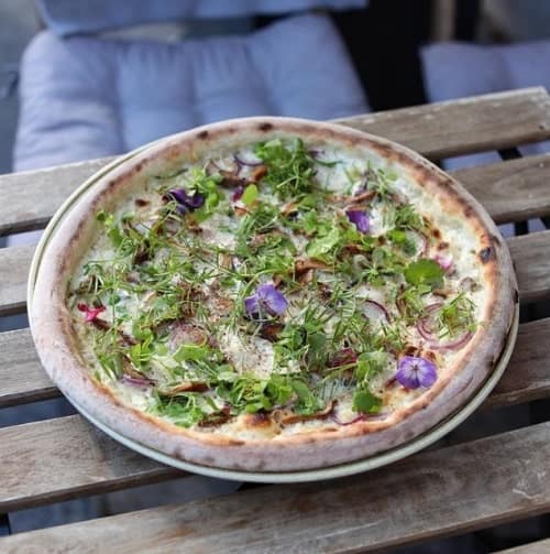 one large round vegan pizza covered in cheese and arugula on a wood table in prague