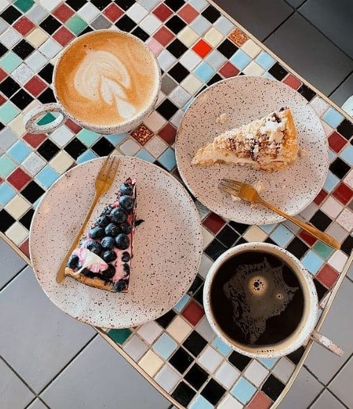 two slices of vegan cake on a colorful square tiled table next to two cups of coffee at eter in warsaw