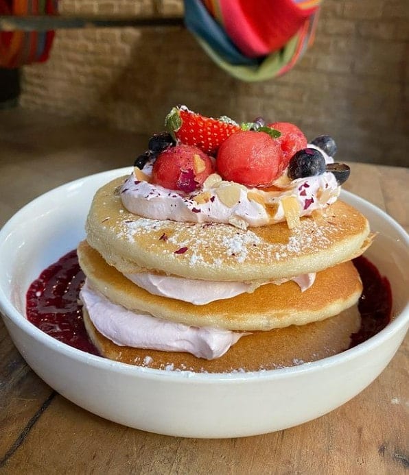 a large golden brown stack of vegan pancakes topped with strawberries at hammock juice in barcelona