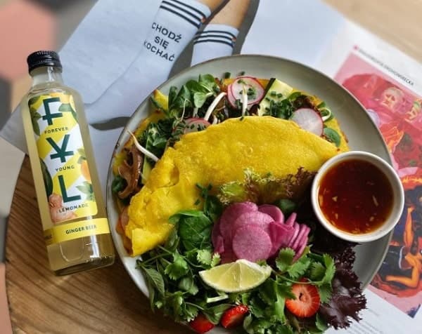 a vegan omelet filled with veggies next to a green salad and a bottle of juice at jaskolka in warsaw