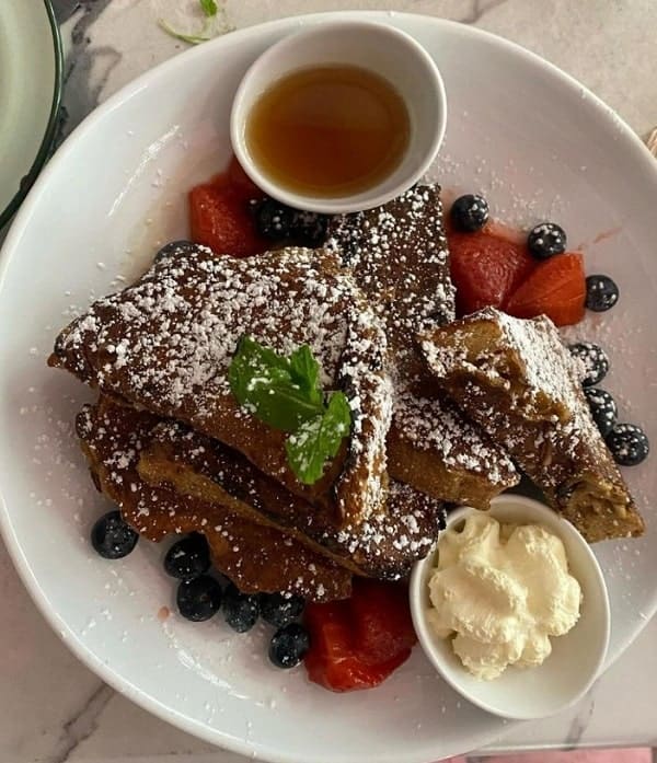 a stack of golden vegan french toast covered in a dusting of white powdered sugar at ladybird in nyc