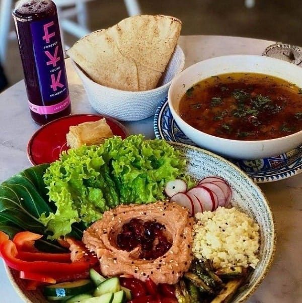 w round bowl filled with leafy greens, hummus, and other veggies next to bread and soup at mango street food in warsaw