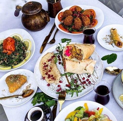 a vegan middle eastern feast - a white clothed tabled filled with plates of falafel, hummus, salad, tea, and more
