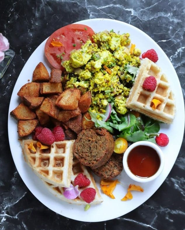 a giant white plate fille with golden vegan waffles, tofu scramble, crispy potatoes and sausage at modern love in brooklyn