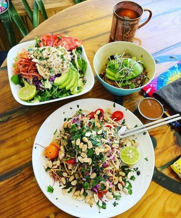 a large bowl of vegan noodle next to a large salad on a wood table at moku roots in maui
