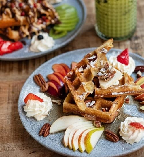 a large stack of golden vegan waffles topped with pecans, apples, and whipped cream in prague