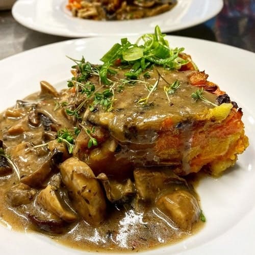 white plate with layed vegan vegetable dish, potatoes covered in a brown gravy in prague