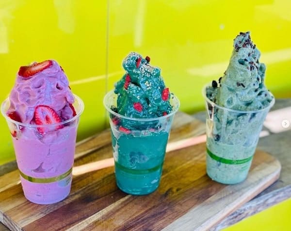 three tall cups filled with vegan softserve in bright purple, mint, and turquoise colors sitting on a wood table at rainbow kitchen in maui