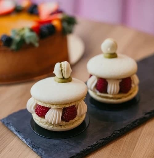 two white vegan macaroons with cream and raspberries in the middle on a black plate in prague