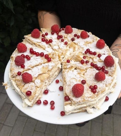 a large flaky vegan  tarte covered in powered sugar and raspberries and filled with cream from slodki bez in warsaw