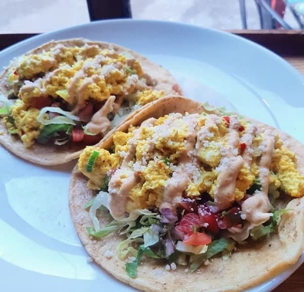 two vegan breakfast tacos with tofu scramble and a creamy sauce on a white plate at urban vegan kitchen in NYC