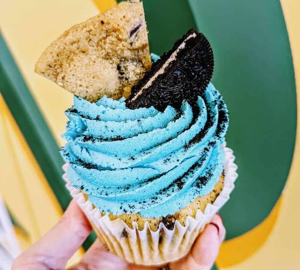 vegan cookie monster cupcake topped with blue buttercream, chocolate chip cookie, and an oreo