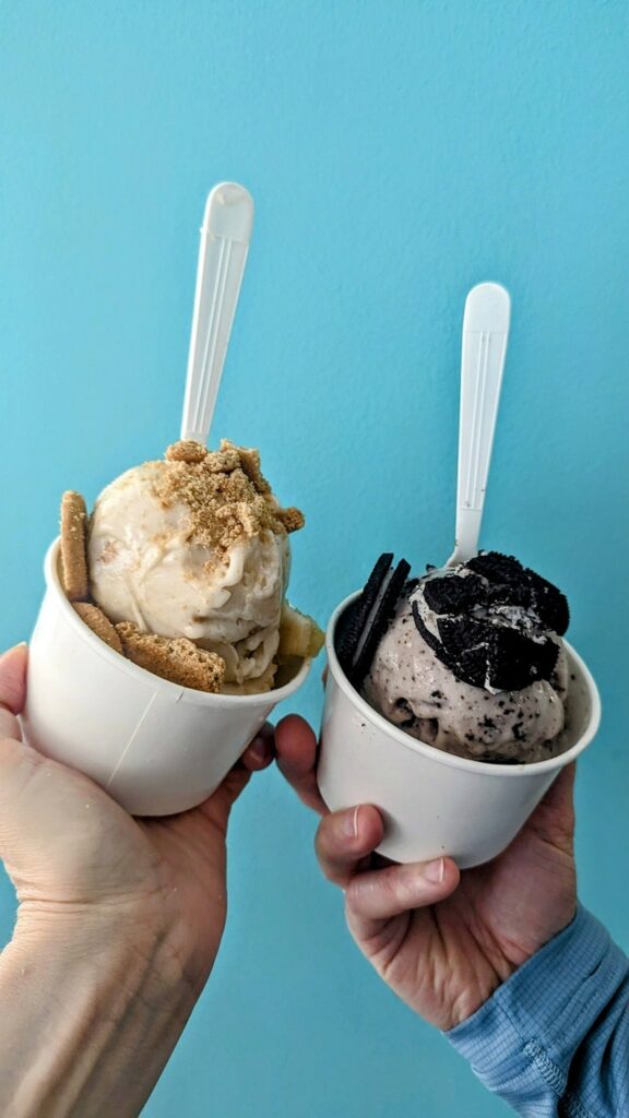 two vegan ice cream sundae topped with vanilla wafers and oreos in front of a teal wall at ifreeze creamery