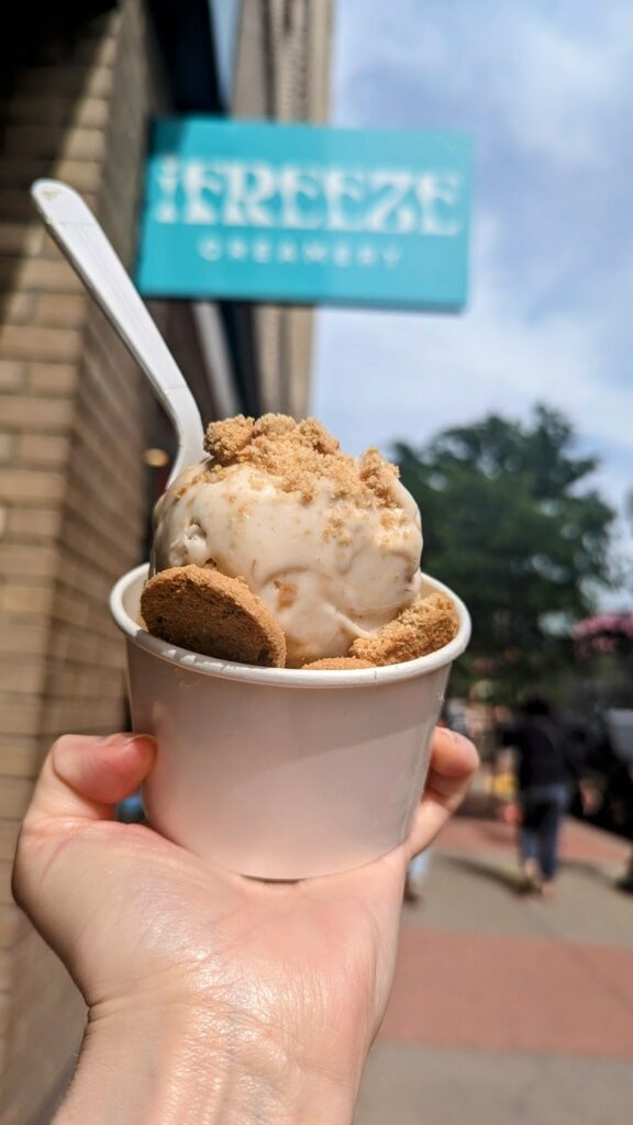 a single vegan banana pudding ice cream sundae held in a white cup in front of the ifreeze creamery sign in detroit