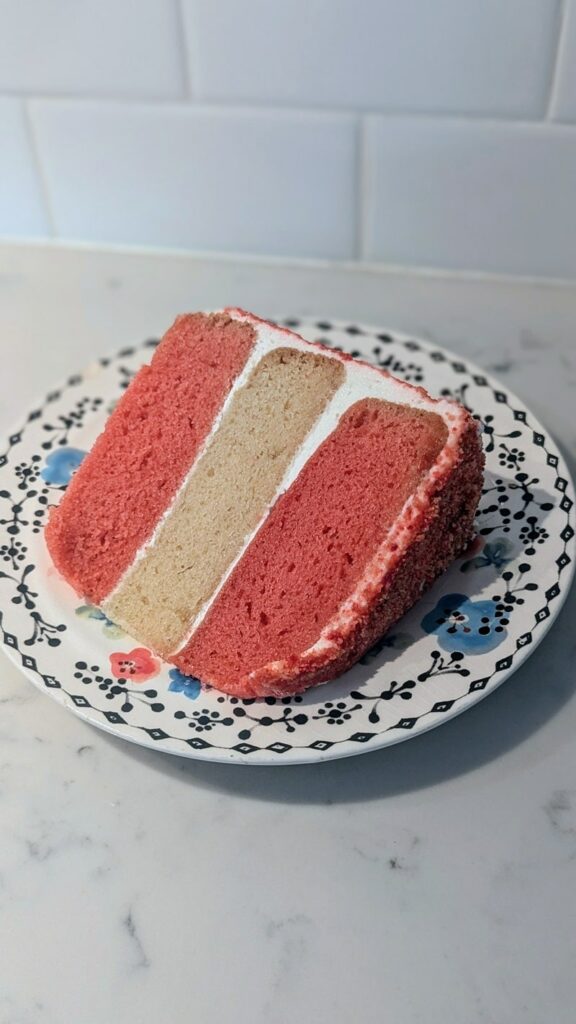 a slice of vegan strawberry cake with layers of pink strawberry cake and vanilla cake on a blue and white plate in detroit