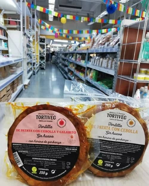 two vegan spanish tortilla held in front of an aisle of vegan products at vegan and bio super market in barcelona