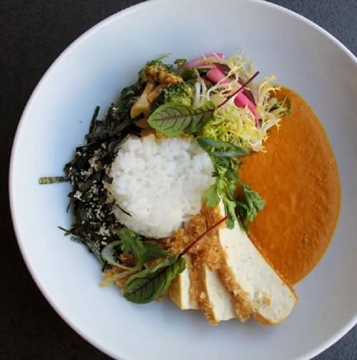 a large white bowl filled with a vegan orange sauce, white rice, tofu, and veggies in prague