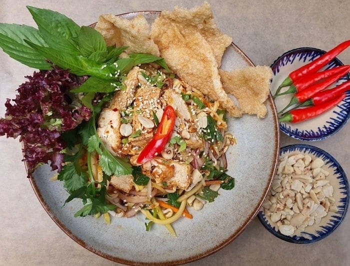 vegan asian noodle bowl with fresh green sail and crispy wontons next to little bowls of nuts and chilis at chum chay in cologne