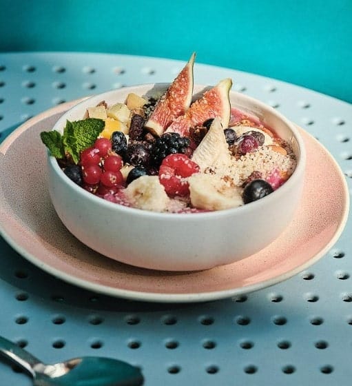 a small white bowl filled with vegan acai and fruit on a turquoise table at green finch in berlin