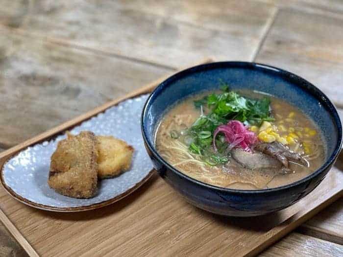 a bowl of vegan ramen topped with green onions on a wooden platter at men impossible in amsterdam
