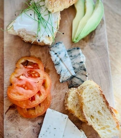 wood vegan cheese board with three kinds of cheese, bread, avocado, and tomato in new york city