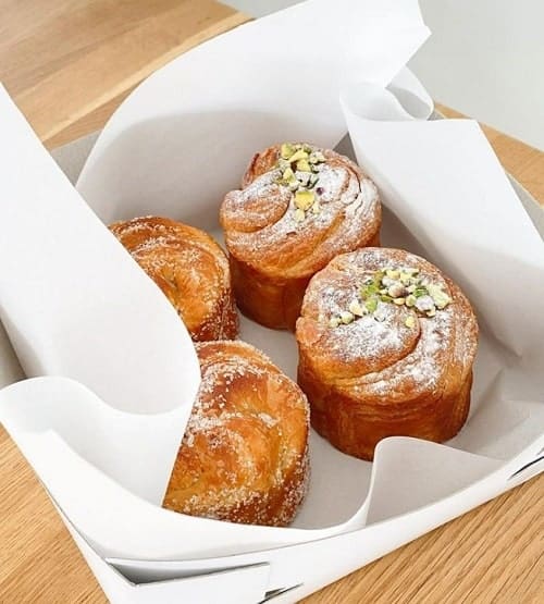 a white take out box filled with four golden vegan pastries from saint jean in amsterdam