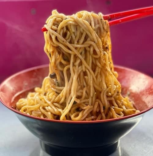 small red round bowl with asian noodles being pulled from above by a pair of chopsticks in new york city