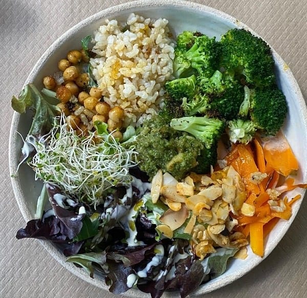 large vegan buddha bowl filled with broccoli, greens, beans and hummus at thank you mother in seville